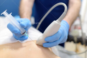 超音波撮影器具と検査用の注射針を手に持ち患者の腹部検査を行っている様子