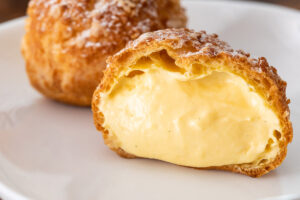 シュークリームが2個あり、1つは断面が見えていて中のクリームがあふれ出しそう。